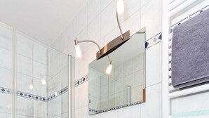 Ein modernes Badezimmer mit einer gläsernen Dusche, einem weißen Waschbecken und einem Spiegel darüber.
