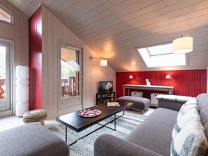 Ein gemütliches Zimmer mit Holzboden, einer roten Akzentwand, einem Esstisch, einer Couch und einem Fenster mit Blick.