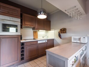 A kitchen with wooden cabinets, a white countertop, a built-in microwave, and a hanging light fixture.