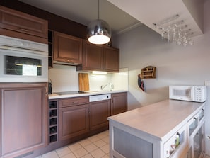 A kitchen with wooden cabinets, a white countertop, a built-in microwave, and a hanging light fixture.