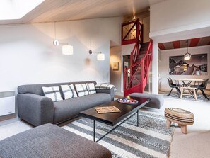 A modern living room with a grey sofa, a coffee table, a striped rug, and a red staircase.