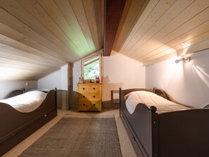 A bedroom with two beds, a dresser, a window, and a wall-mounted light fixture.