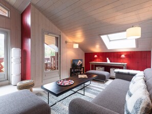 A cozy room with a wooden ceiling, a red accent wall, a dining table, a sofa, and a window with a view.