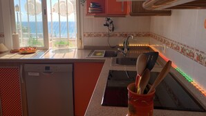 A kitchen with a view of the sea, a dishwasher, a sink, and a countertop with a bowl of tomatoes.