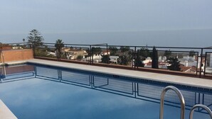 A rooftop swimming pool with a view of the cityscape and the sea.