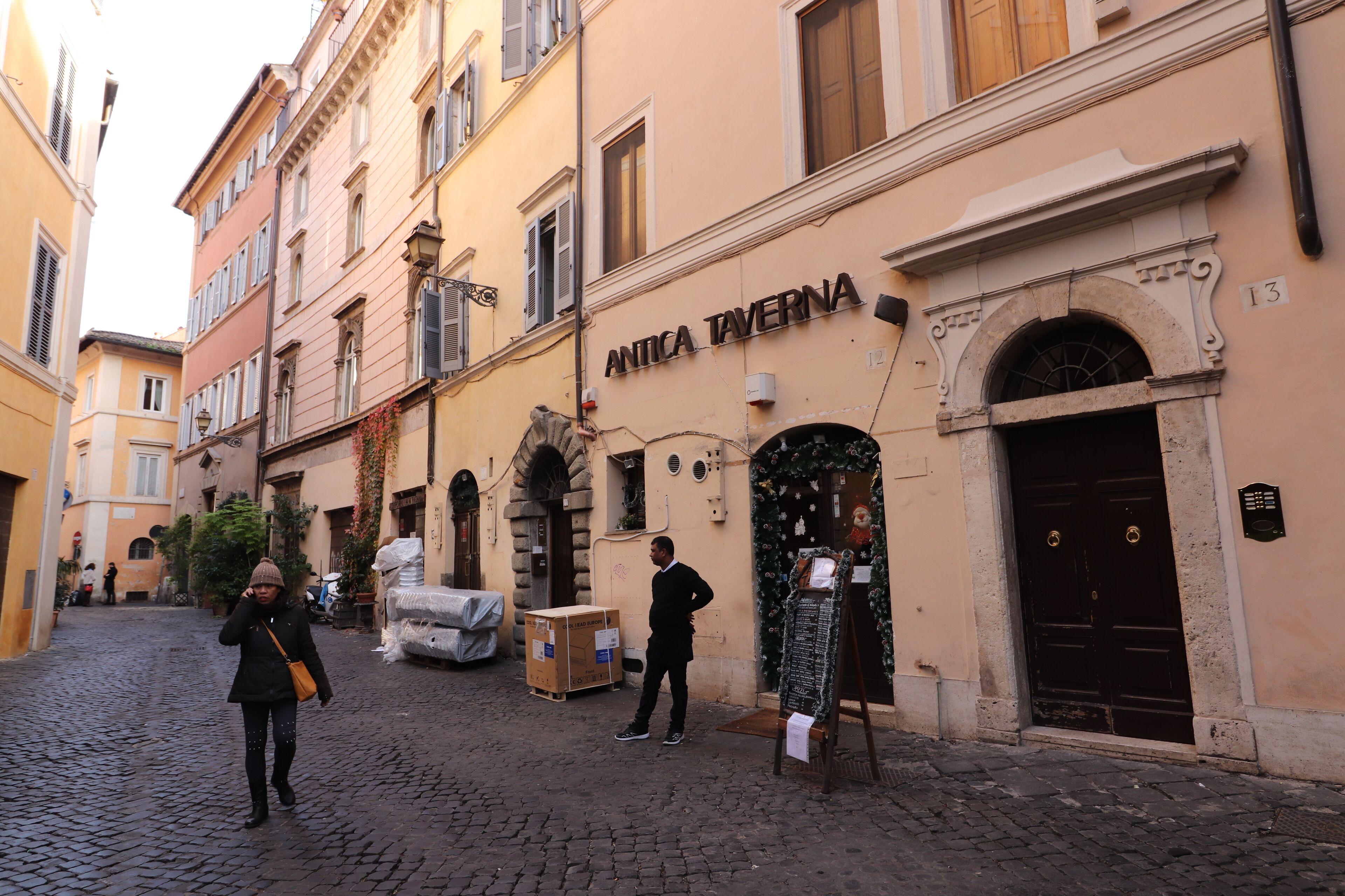 Una strada acciottolata con edifici, uno dei quali reca la scritta "ANTICA TAVERNA".
