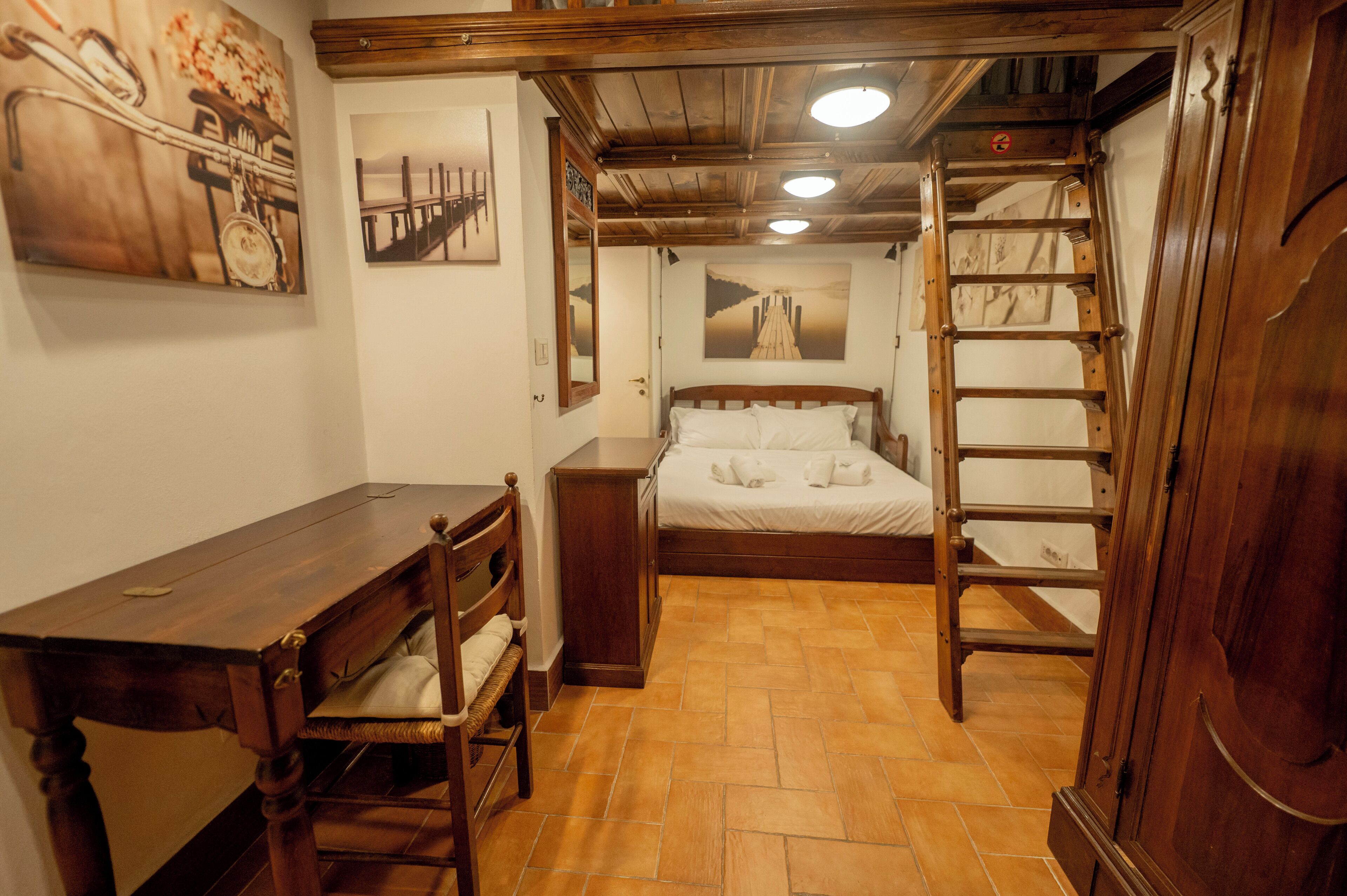 A bedroom with a wooden bed, a desk, a chair, and a ladder.