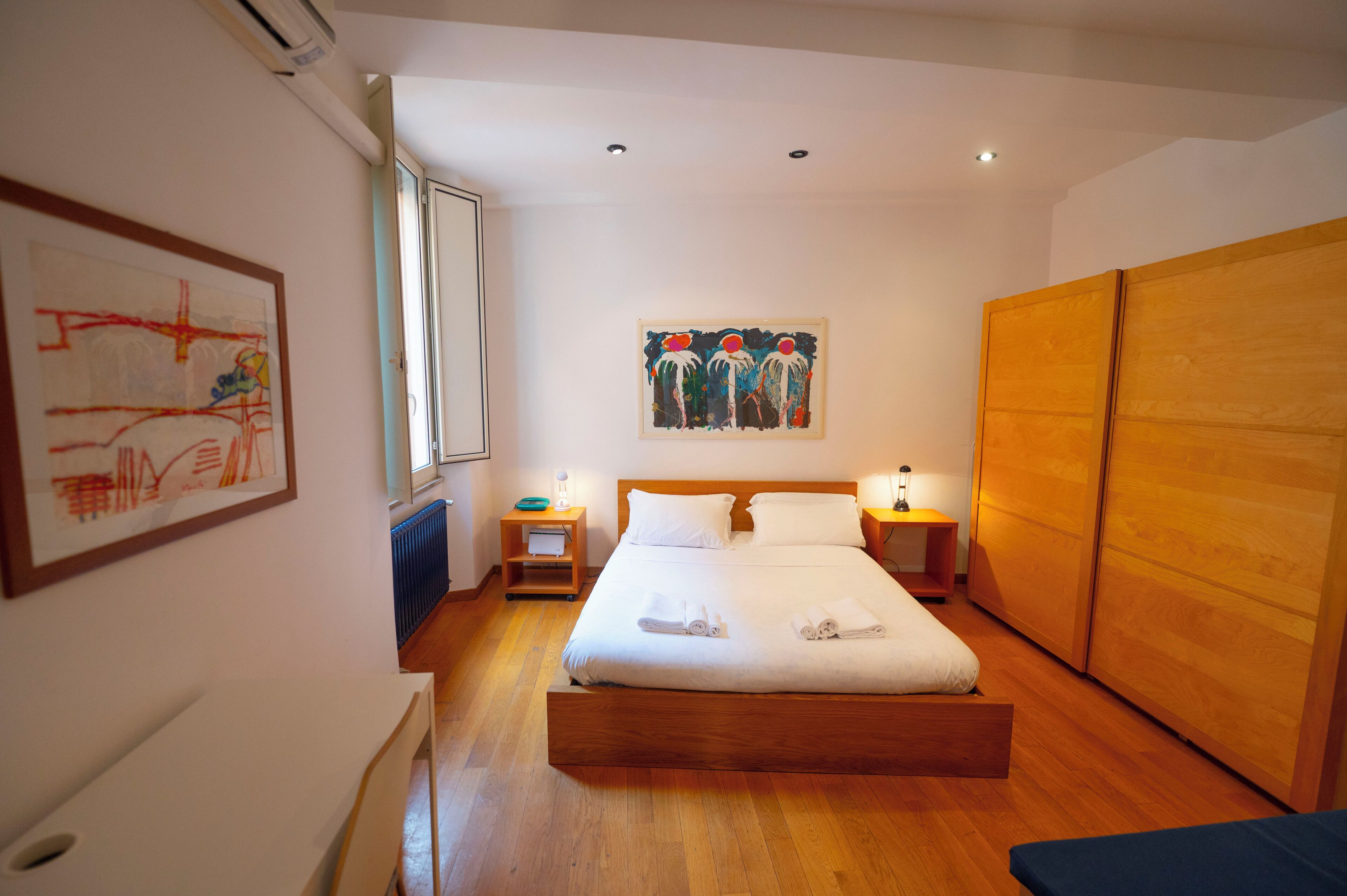 Un dormitorio ordenado con una cama grande, un armario de madera y obras de arte en las paredes.