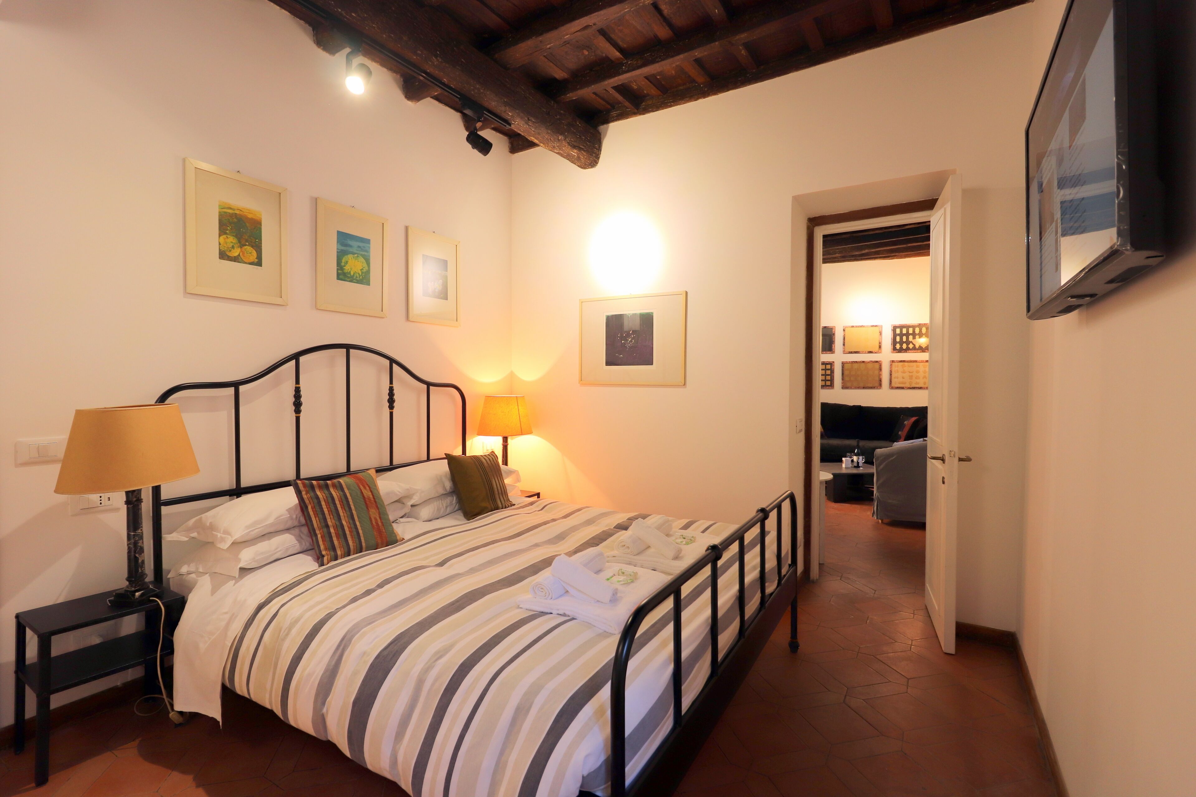 Une chambre d’hôtel équipée d’un lit, de lampes de chevet, d’un téléviseur à écran plat et d’un couloir menant à un espace de vie.