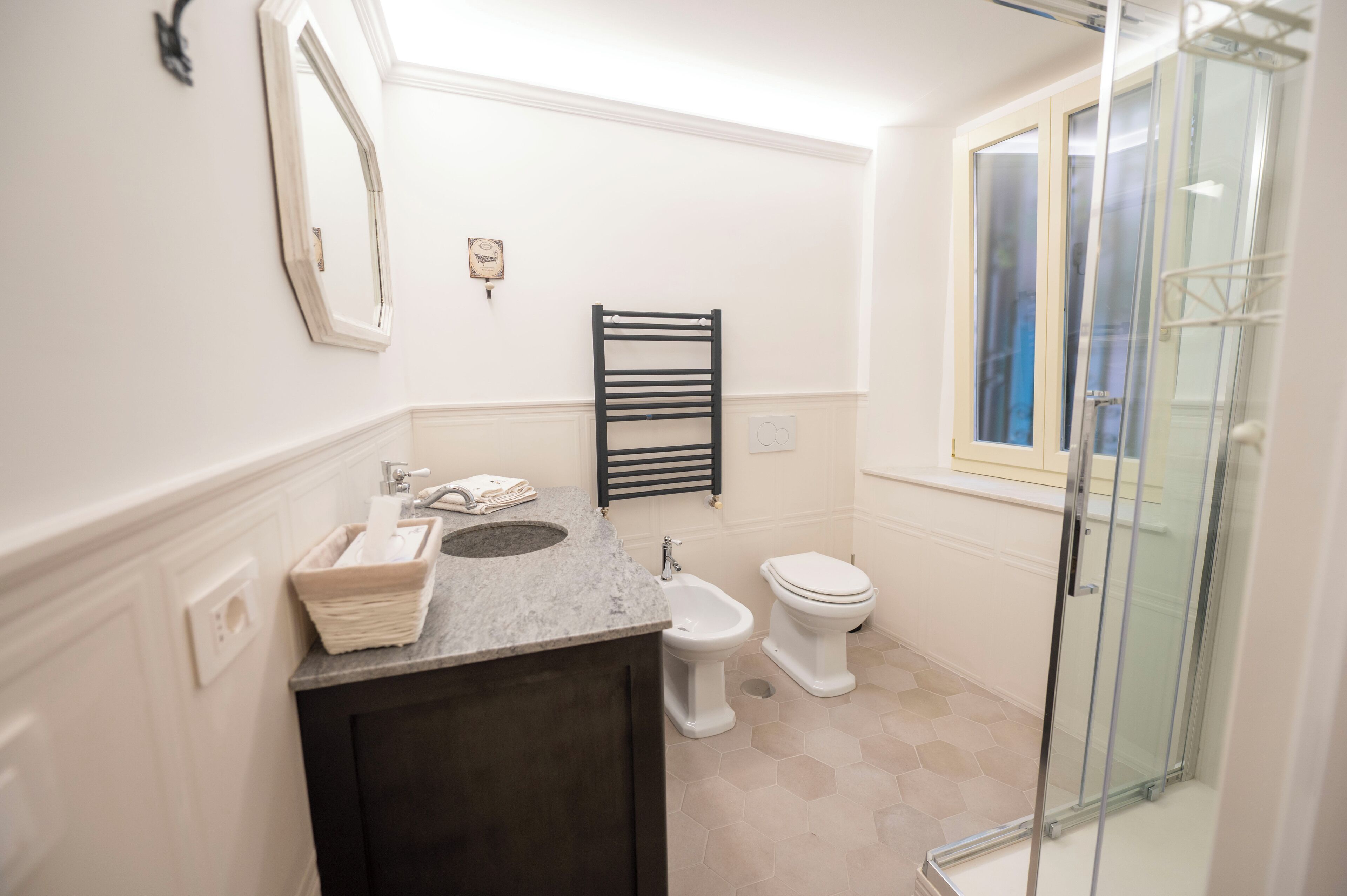 A bathroom with a sink, mirror, towel rack, bidet, toilet, and a glass shower enclosure.