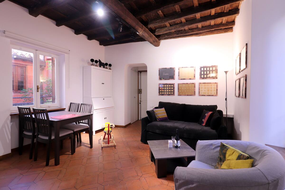 A living room with a dining table, chairs, a sofa, and a coffee table. There is a window with a view of the outside.