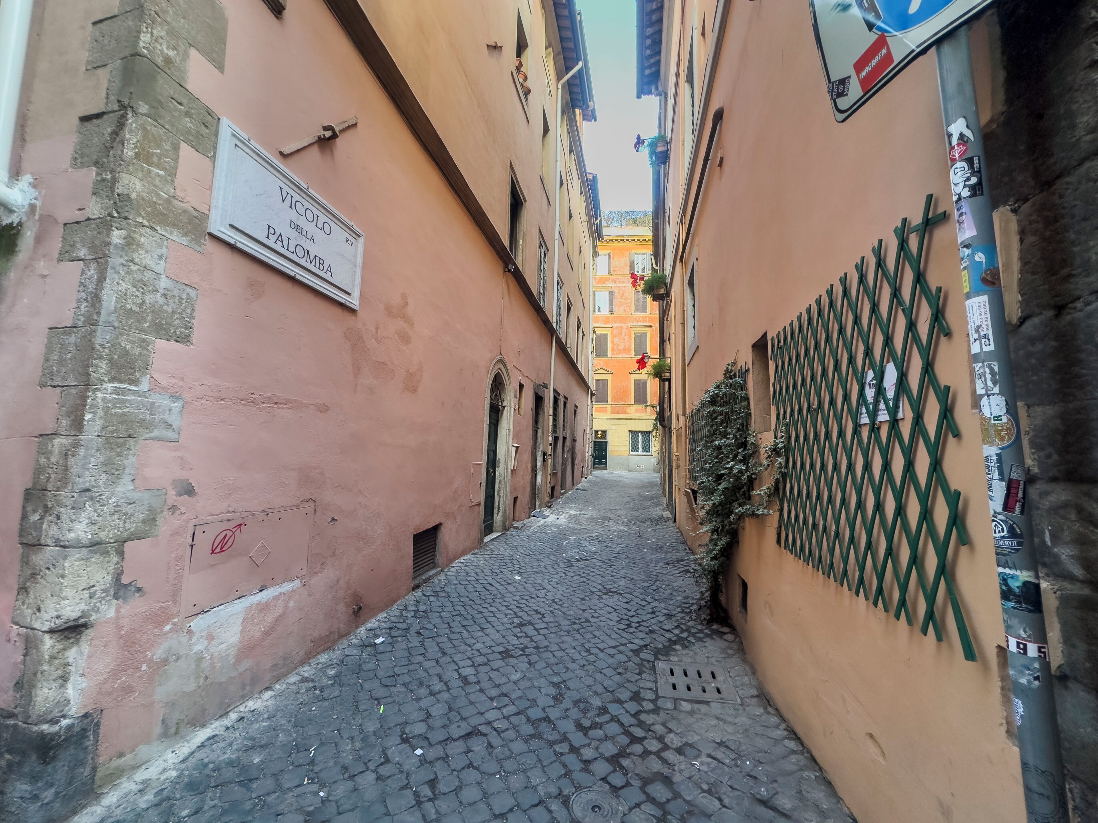 A narrow cobblestone alley with buildings on either side, one with a sign reading "Vicolo della Palomba."