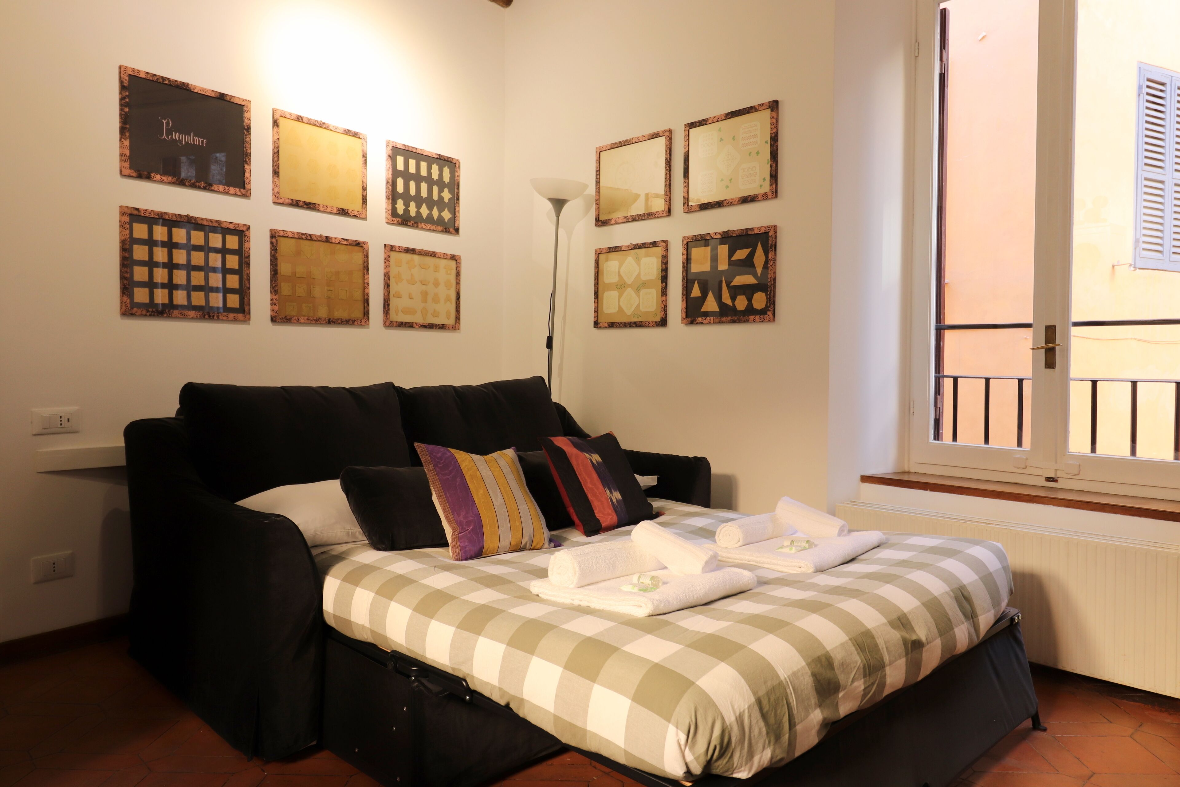 A bedroom with a bed, a black sofa, and a window with shutters.