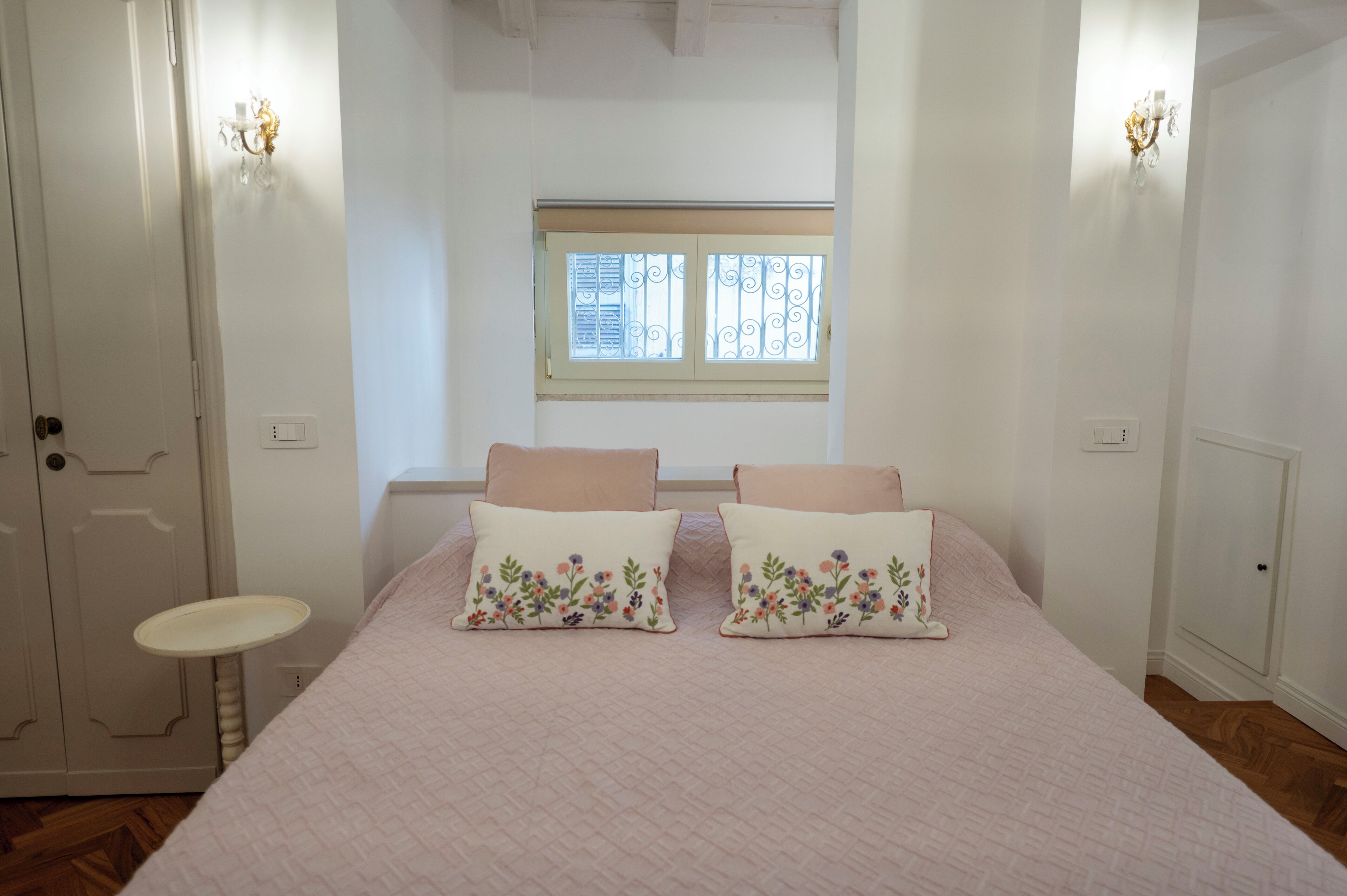A bedroom with a bed, two pillows, a nightstand, a window, and a door.