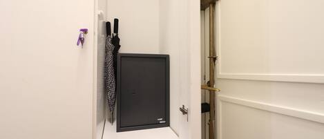 Un couloir étroit avec une porte blanche sur la droite, une petite étagère blanche sur laquelle se trouve un objet noir, et un porte-clés violet.