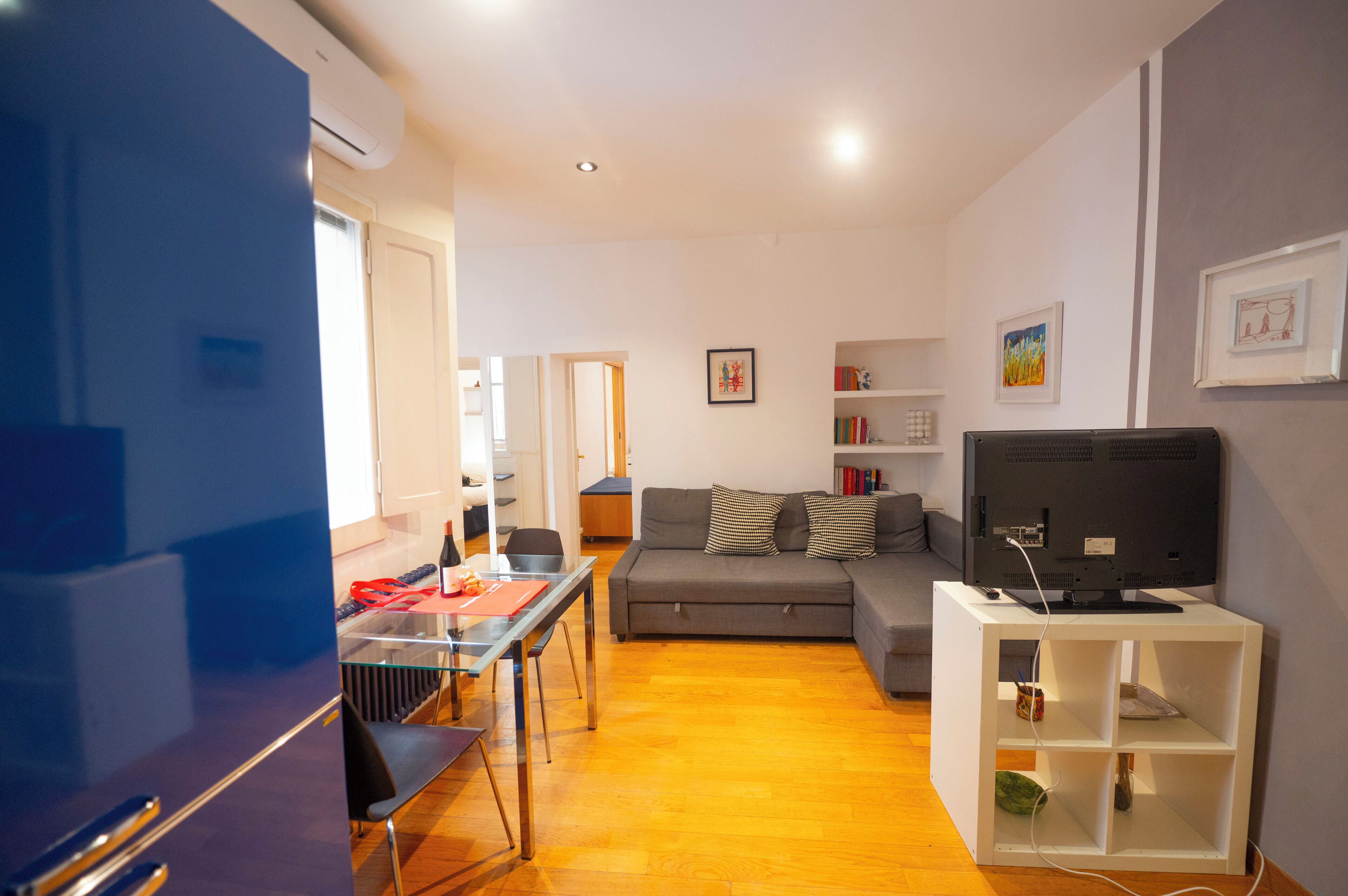 A living room with a sofa, a TV on a stand, and a dining area with a table and chairs.
