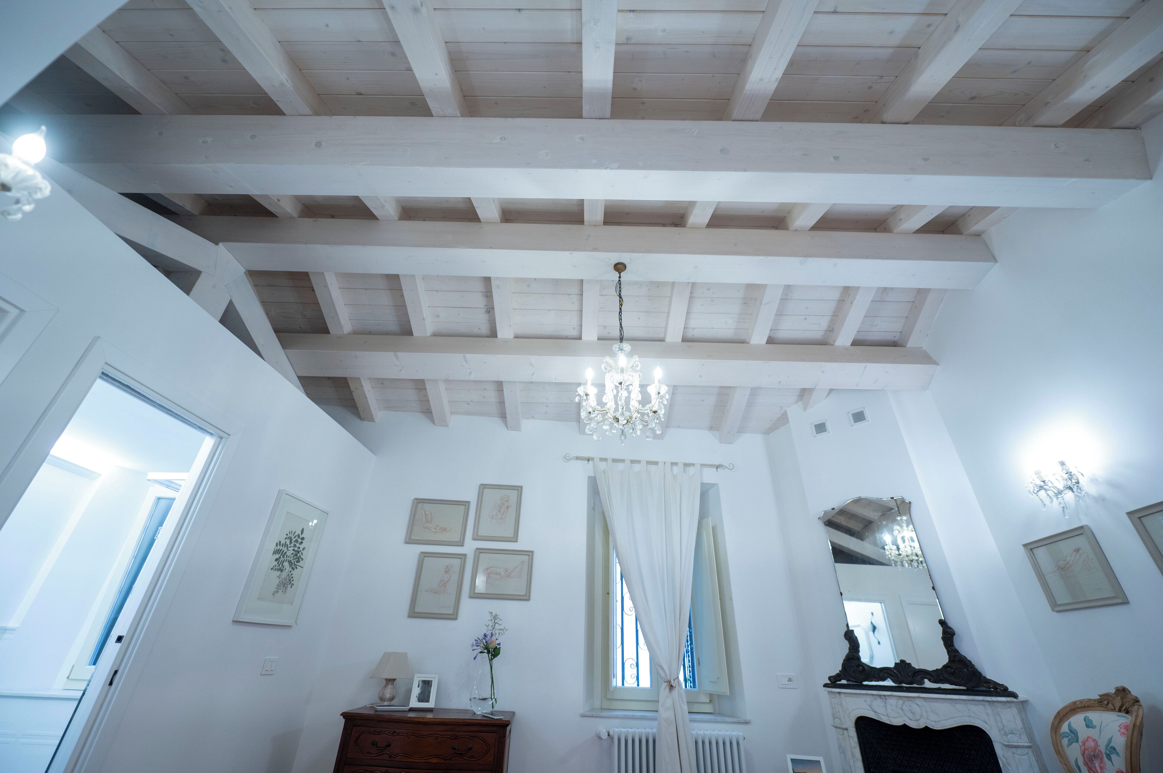 A room with a high wooden ceiling, a chandelier, a fireplace, and framed artwork on the walls.