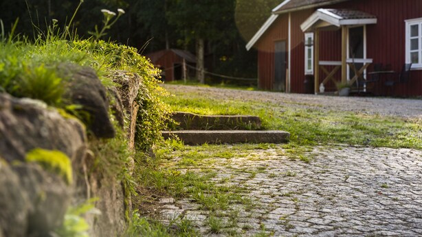 A cobblestone path leading to a red building with a porch. - Cozy cottage in the countryside, surrounded by nature (Västra Götalands län)