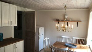 A kitchen with white cabinets, a wooden countertop, a white refrigerator, and a dining table with white chairs. There is a chandelier above the table. - Cozy cottage in the countryside, surrounded by nature (Västra Götalands län)