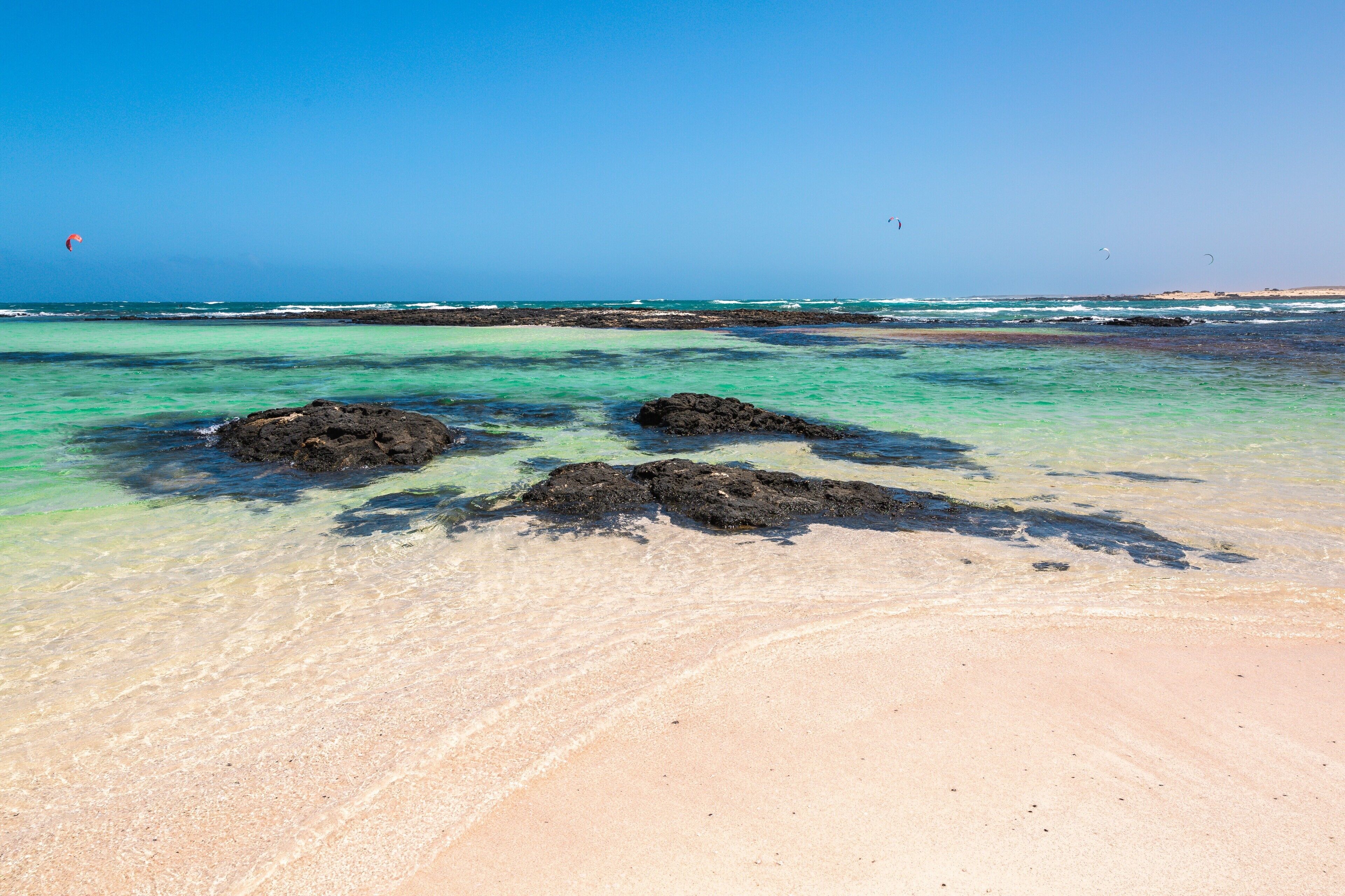 Une plage avec une eau turquoise et limpide, des rochers visibles et une côte qui s’étend au loin.