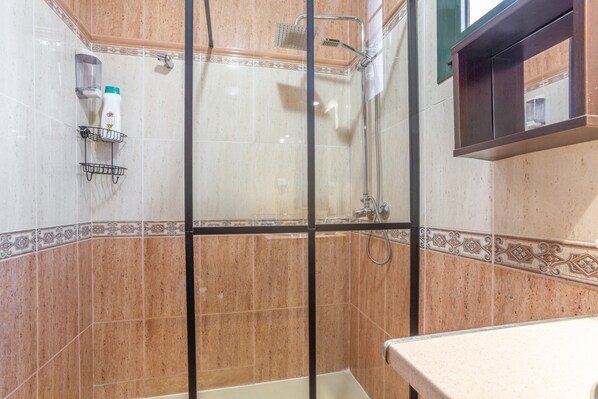 A shower with a glass door, a towel rack, and a bottle of shampoo.