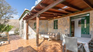 Un patio techado con paredes de piedra, techo de madera y una mesa con sillas.
