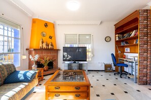 A living room with a sofa, coffee table, TV, fireplace, bookshelf, and a desk with chair.