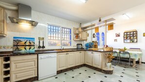 A kitchen with a dishwasher, cabinets, a window with bars, a sink, and a dining area with chairs. - Holiday Home “Milestone House” with Pool, Terrace, Balcony, Air Conditioning & Wi-Fi (Rincon de la Vicoria)