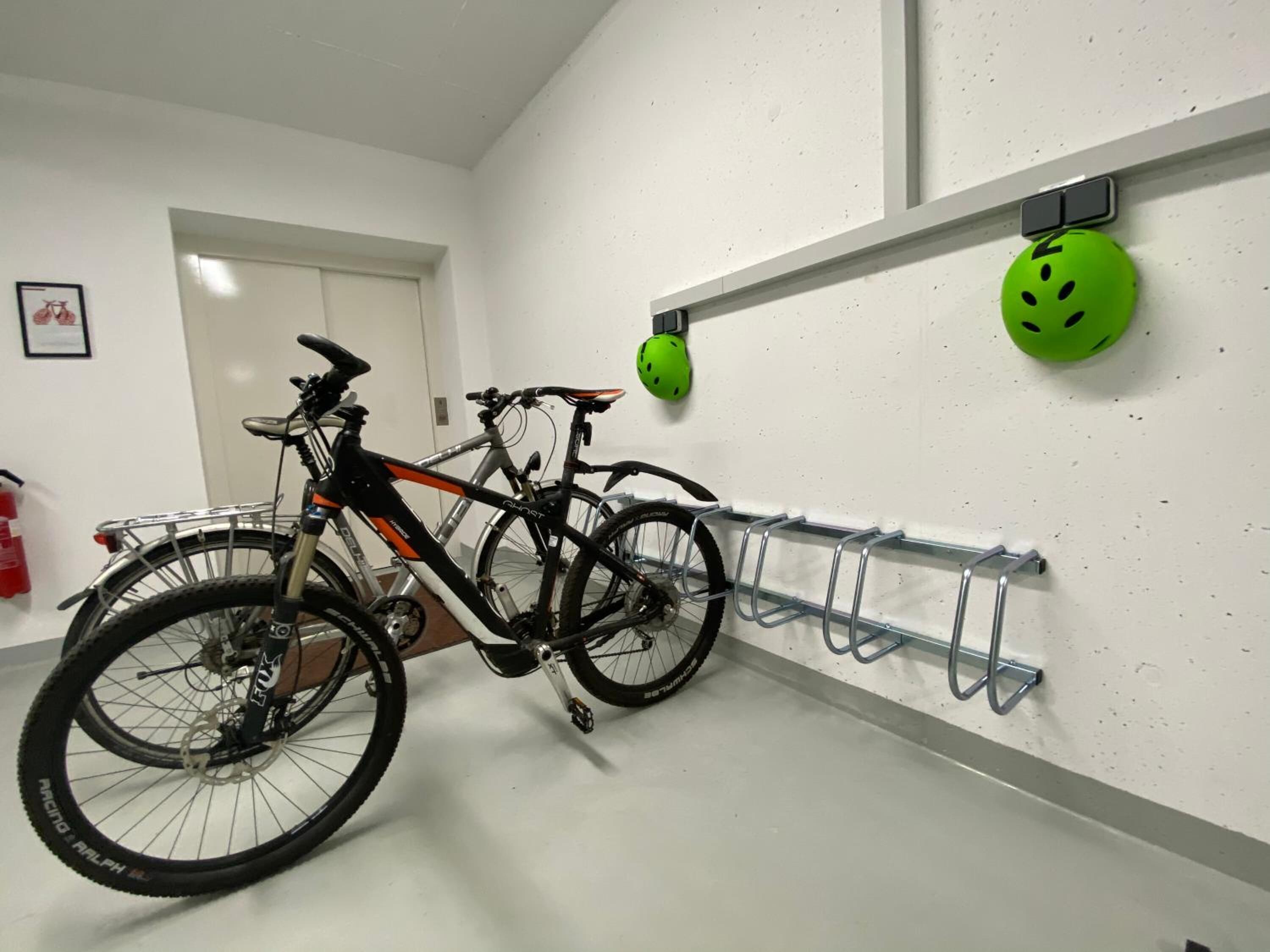 A bicycle parked next to a wall-mounted bike rack with helmets hanging above.