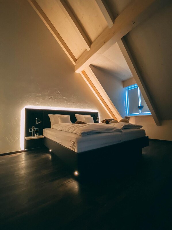 Un dormitorio con techo inclinado, una cama, una mesita de noche y un ventanal.