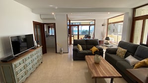 Una sala de estar con televisión, sofás, una mesa de centro y una cocina al fondo.