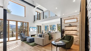 Un salón comedor amplio con techo alto, ventanas grandes, chimenea y un área de descanso acogedora.