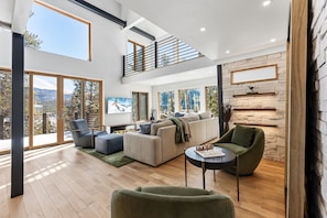 A spacious living room with a high ceiling, large windows, a fireplace, and a cozy seating area.