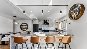 Una cocina moderna con una isla central, iluminación colgante y un reloj de pared grande.
