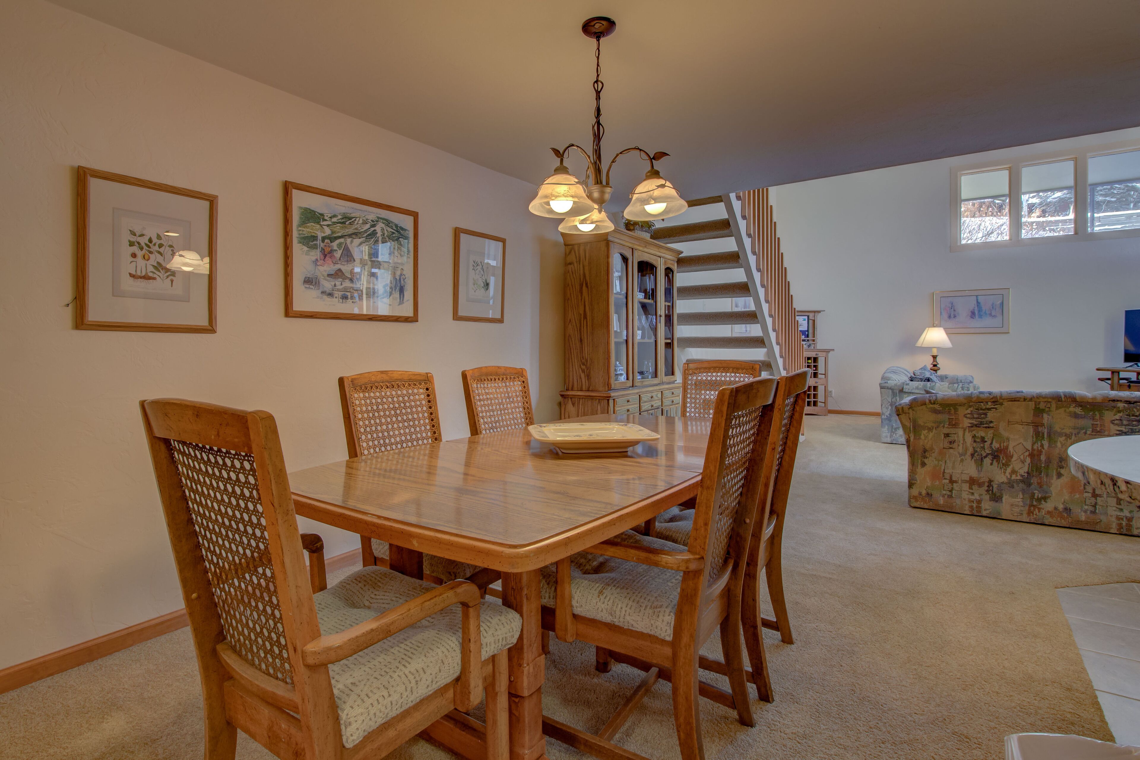 A dining area with a wooden table and chairs, a staircase, and a couch in a living room.