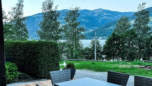 Patio esterno con tavolo e sedie, vista su un lago e montagne.