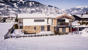 Una casa moderna de dos pisos con fachada de piedra y ventanas amplias, rodeada de montañas nevadas.