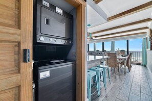 A kitchen with a black stove and a view of a balcony with wicker furniture and a view of the sea. - Island Winds East 401 | Gulf Front Walk to HangOut | Beach Getaways (Gulf Shores)