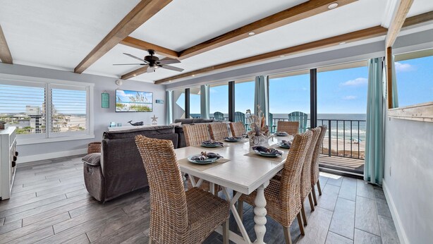 A dining area with a white table and wicker chairs, large windows with a view of the beach, and a ceiling fan. - Island Winds East 401 | Gulf Front Walk to HangOut | Beach Getaways (Gulf Shores)