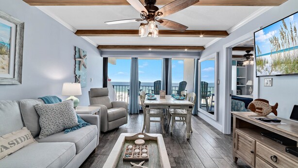 Un vaste salon avec vue sur l’océan, doté d’un ventilateur de plafond et d’un coin repas avec une table et des chaises.