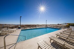 A swimming pool with sunbathing chairs and a fence, surrounded by a clear sky. - Island Winds East 402 Beachfront Condo | Steps to HangOut! | My Beach Getaways (Gulf Shores)