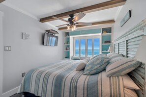 A bedroom with a bed, a ceiling fan, a window with blinds, and a shelf with decorative items.
