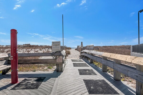 A wooden boardwalk leading to a beach with a 'Leave Only Trash' sign and a 'No Glass on the Beach' sign.