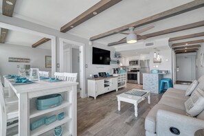 Amplia sala de estar con una mesa de comedor para cuatro, un sofá y una cocina al fondo.