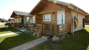 A wooden cabin with a porch, a small deck, and a window with a heart-shaped decoration.
