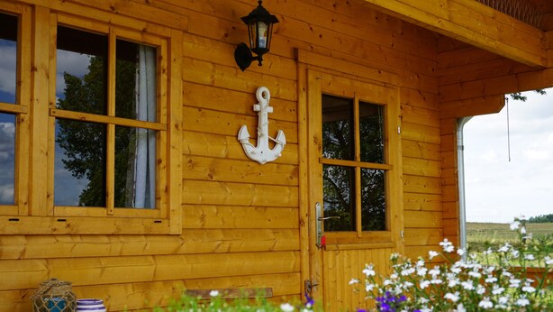 A wooden cabin with large windows, an anchor decoration, and a table with a basket and bowls.