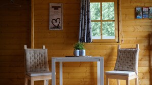 A wooden cabin interior with two upholstered chairs, a small table, and a window with curtains.