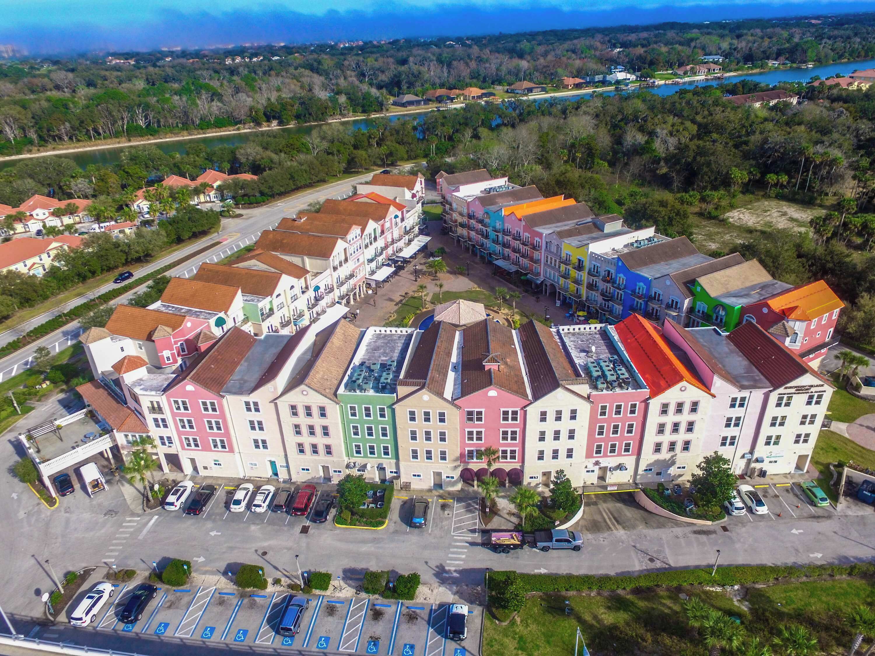 A multi-story hotel with colorful facades, a parking lot, and a view of a lake.