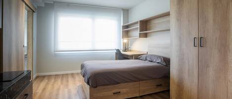 A modern bedroom with a bed, a desk, and built-in wooden shelving.