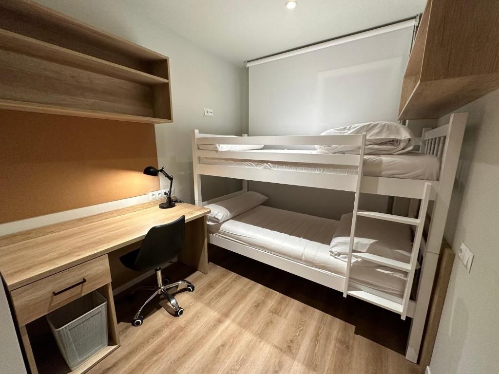 Una cama individual superpuesta con escritorio, silla, un estante pequeño y una ventana.